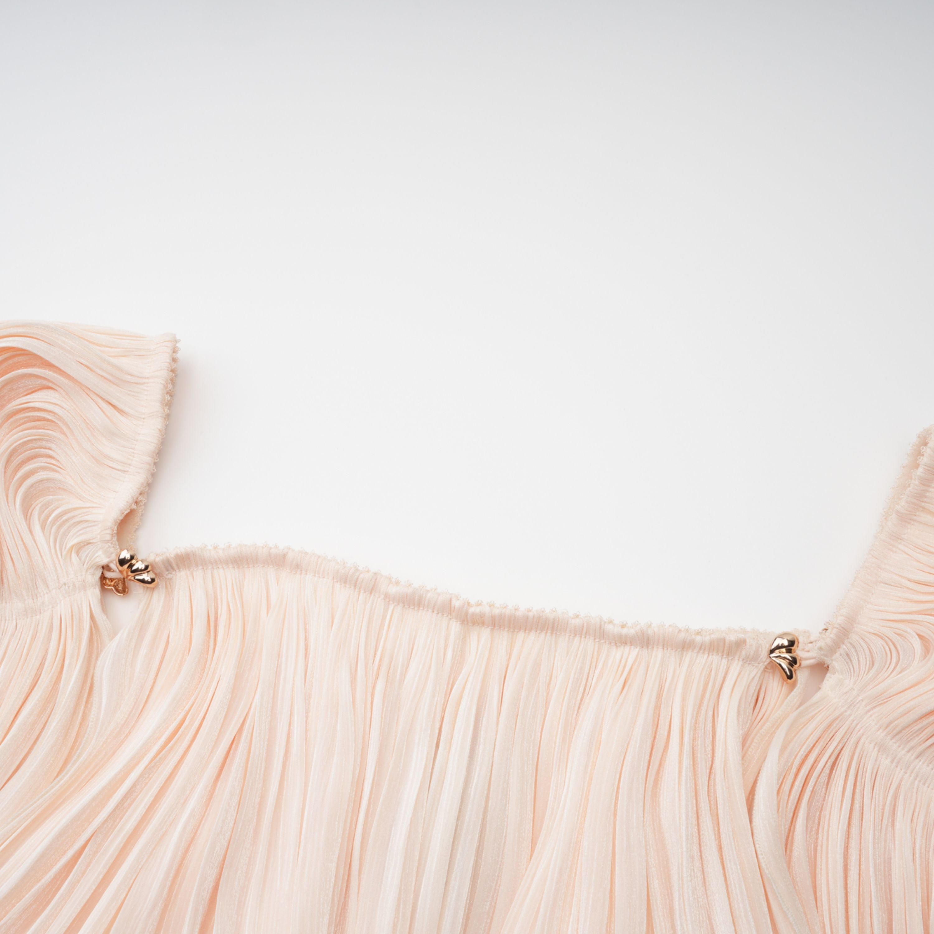 Cream plissé mini dress with a square neckline, structured puff sleeves, and a draped ruffled skirt