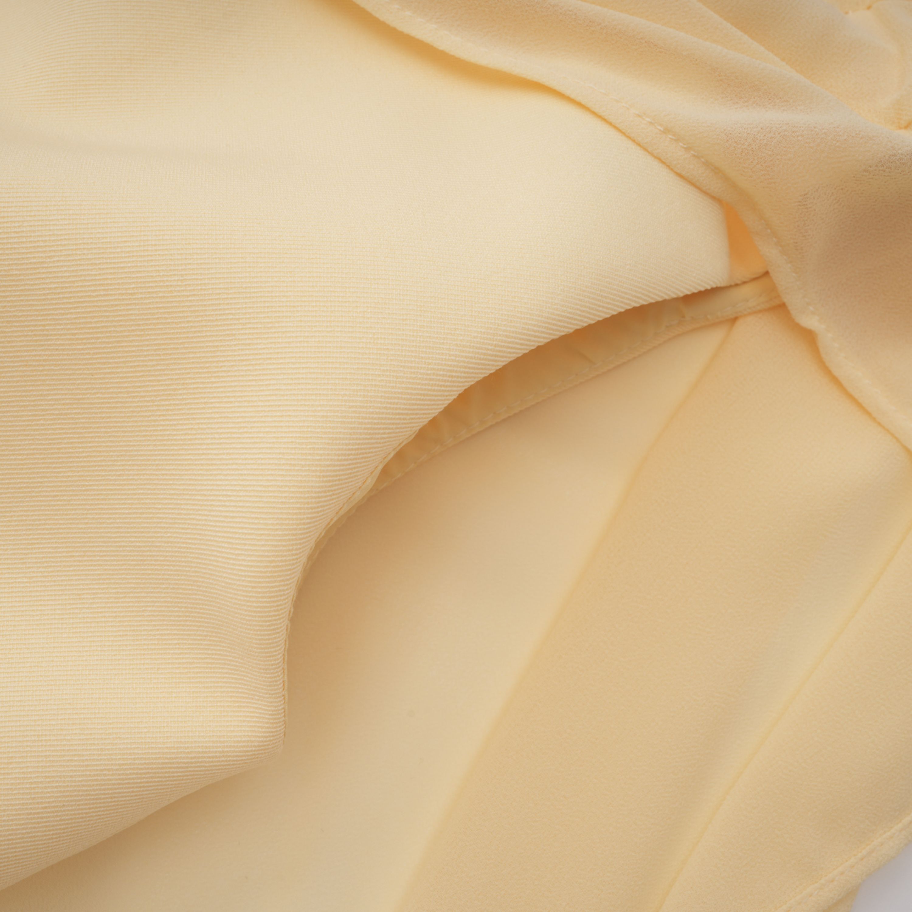 Pale yellow top and trousers set with an asymmetric blazer bodice, draped sheer neckline, and cape panels