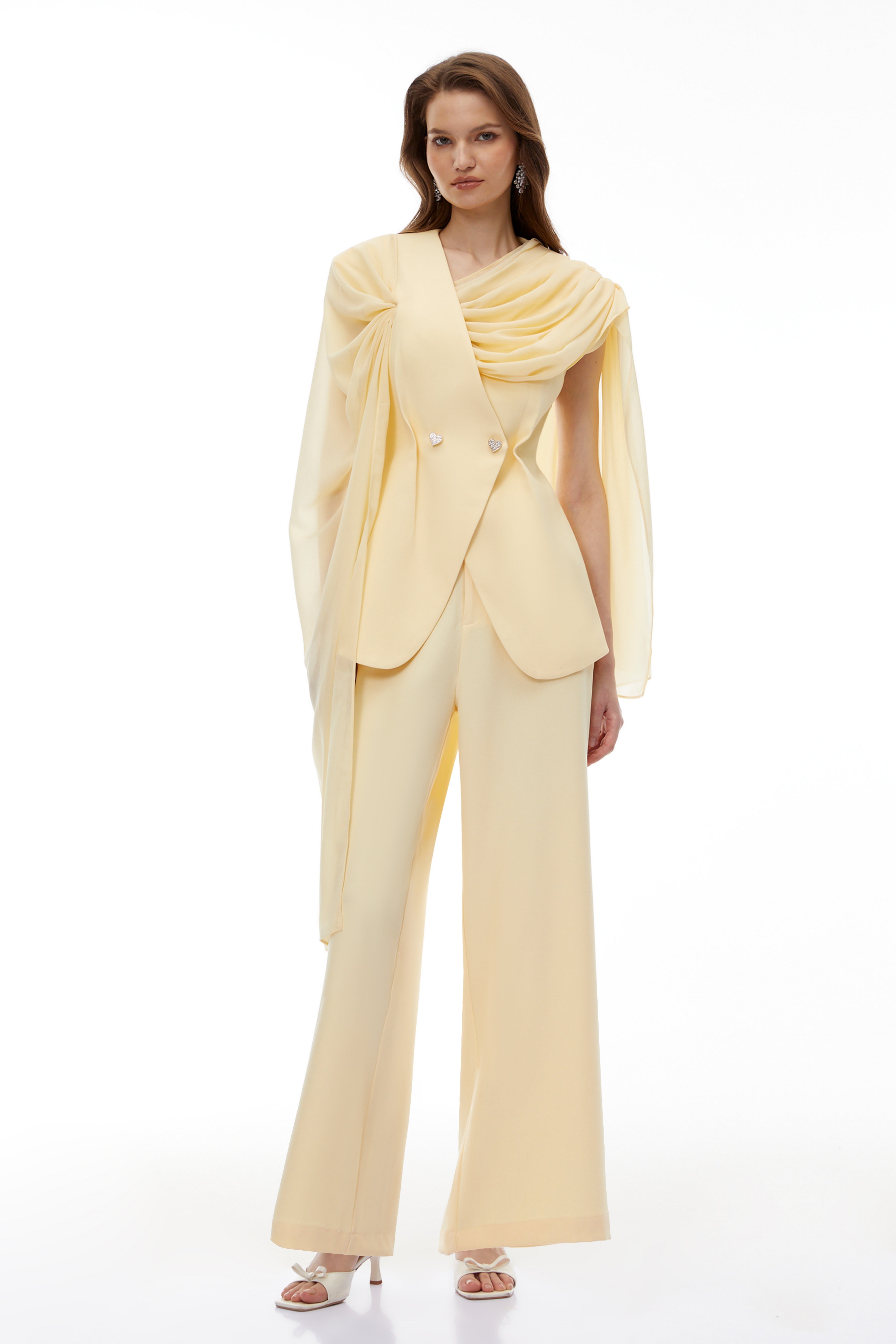Pale yellow top and trousers set with an asymmetric blazer bodice, draped sheer neckline, and cape panels