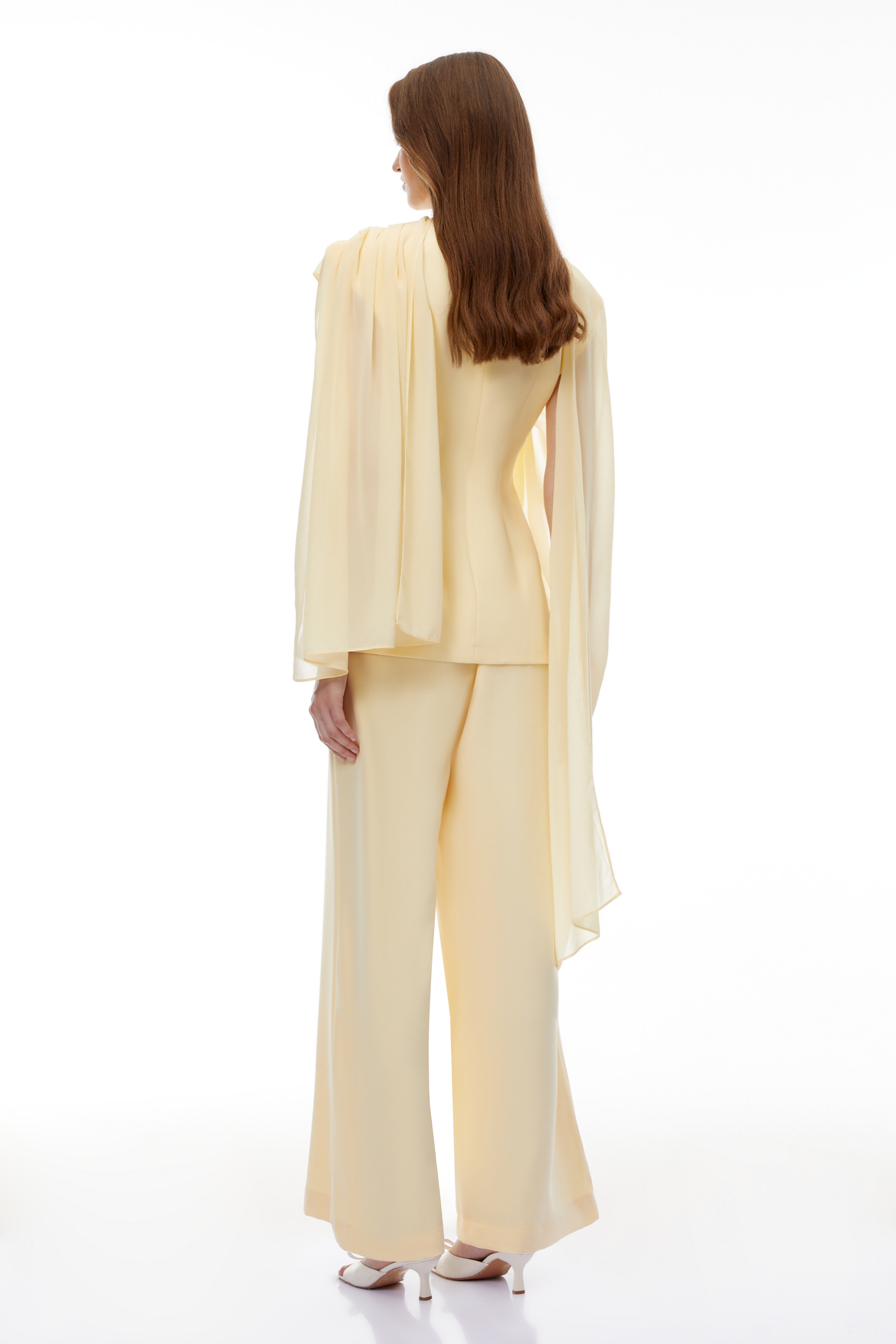 Pale yellow top and trousers set with an asymmetric blazer bodice, draped sheer neckline, and cape panels