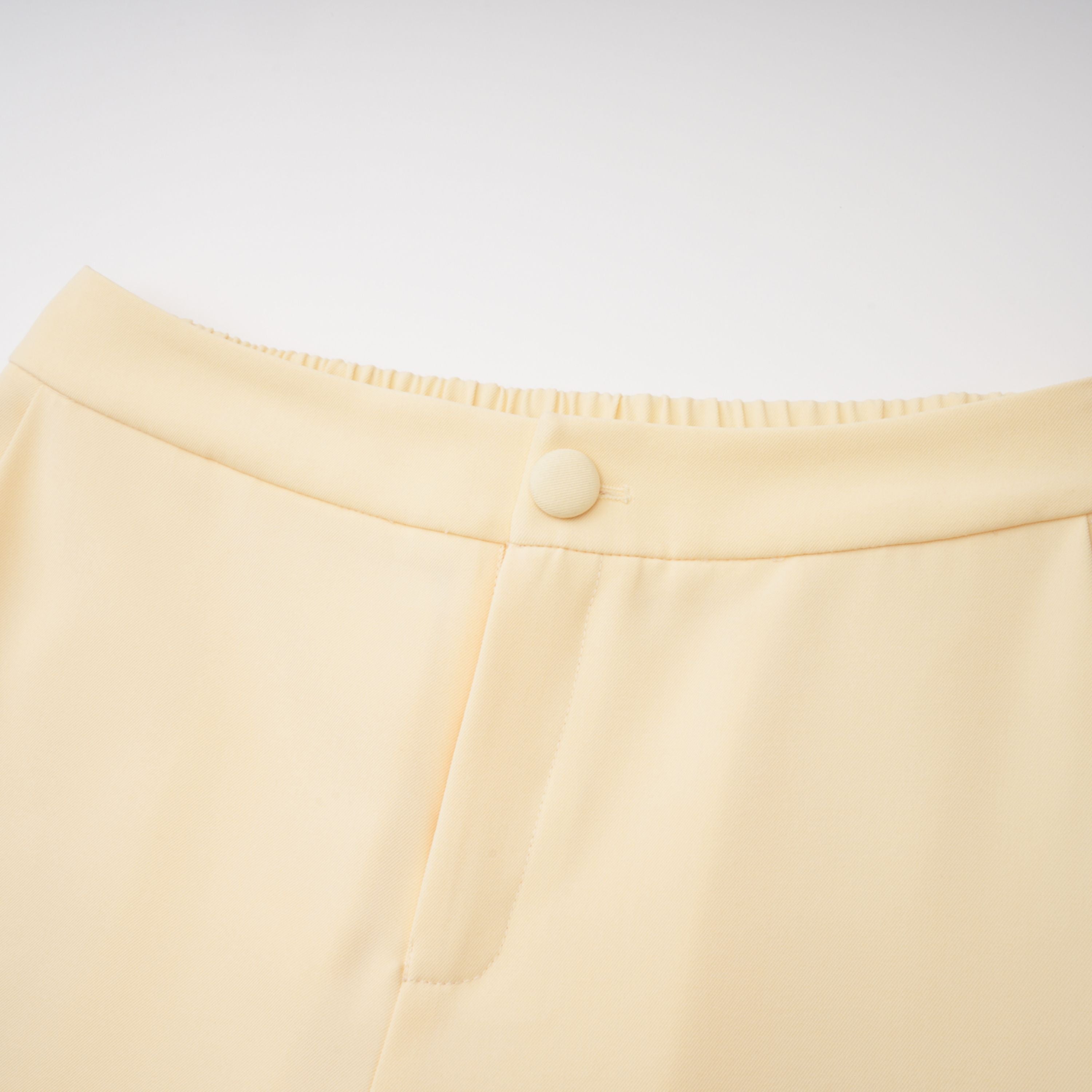 Pale yellow top and trousers set with an asymmetric blazer bodice, draped sheer neckline, and cape panels