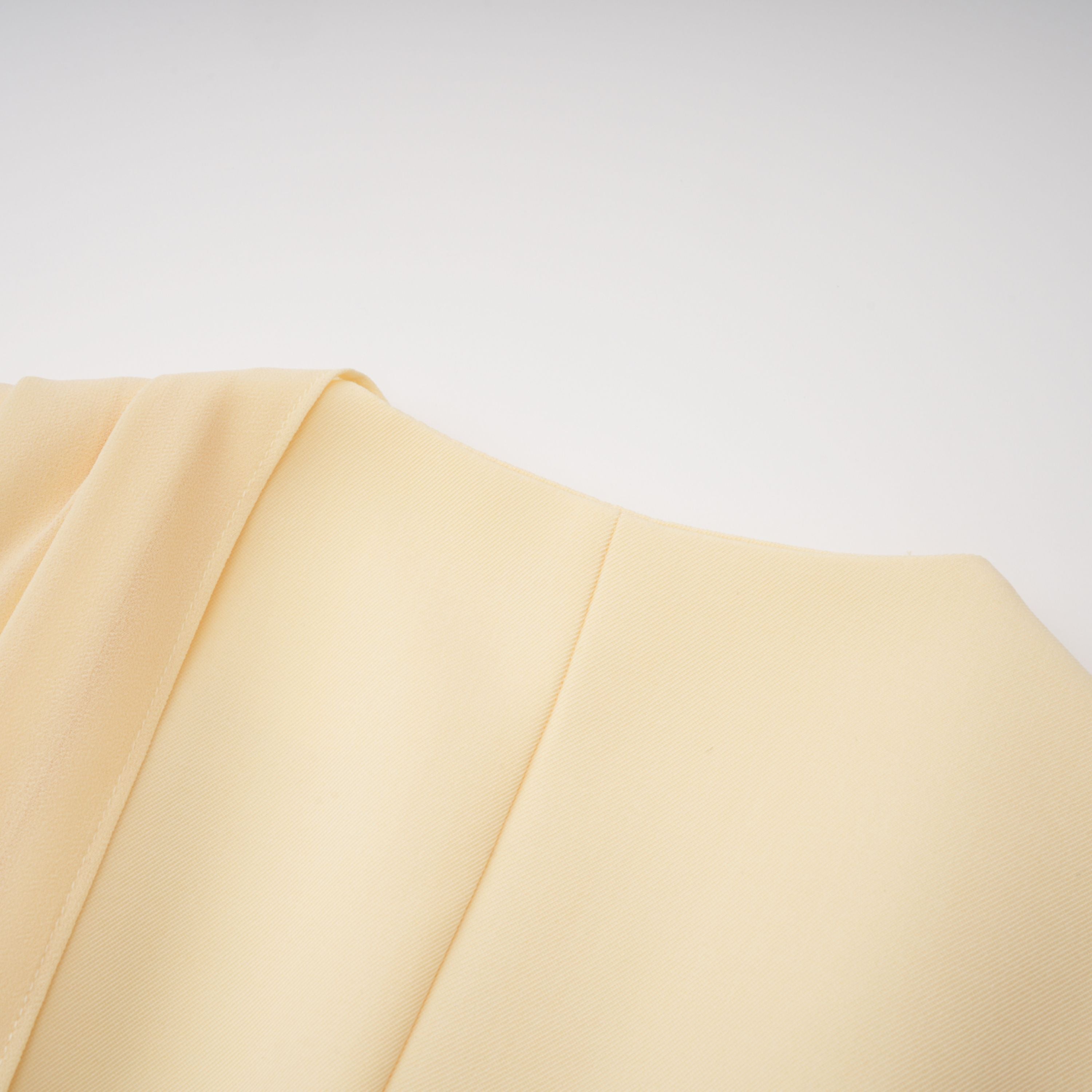 Pale yellow top and trousers set with an asymmetric blazer bodice, draped sheer neckline, and cape panels
