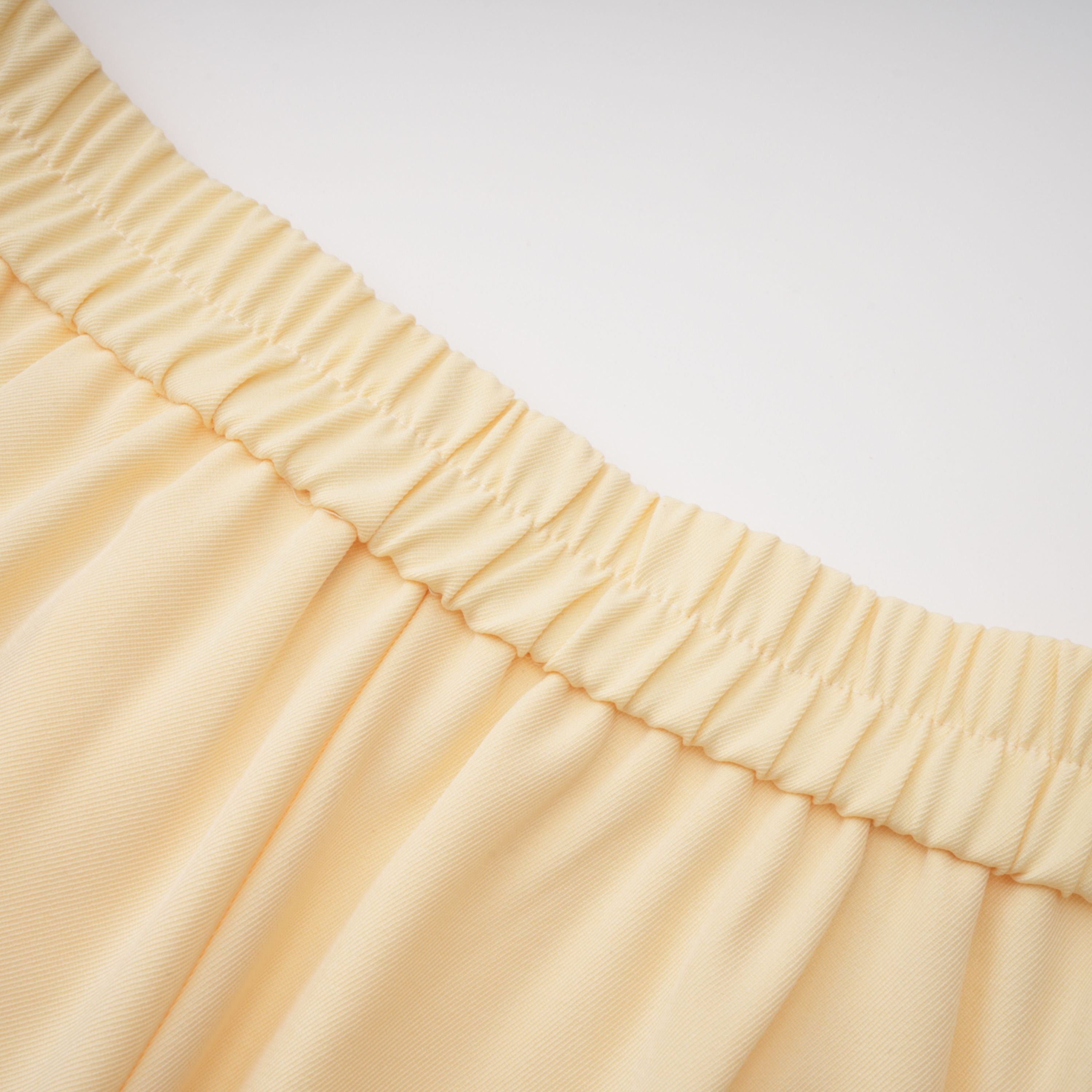Pale yellow top and trousers set with an asymmetric blazer bodice, draped sheer neckline, and cape panels