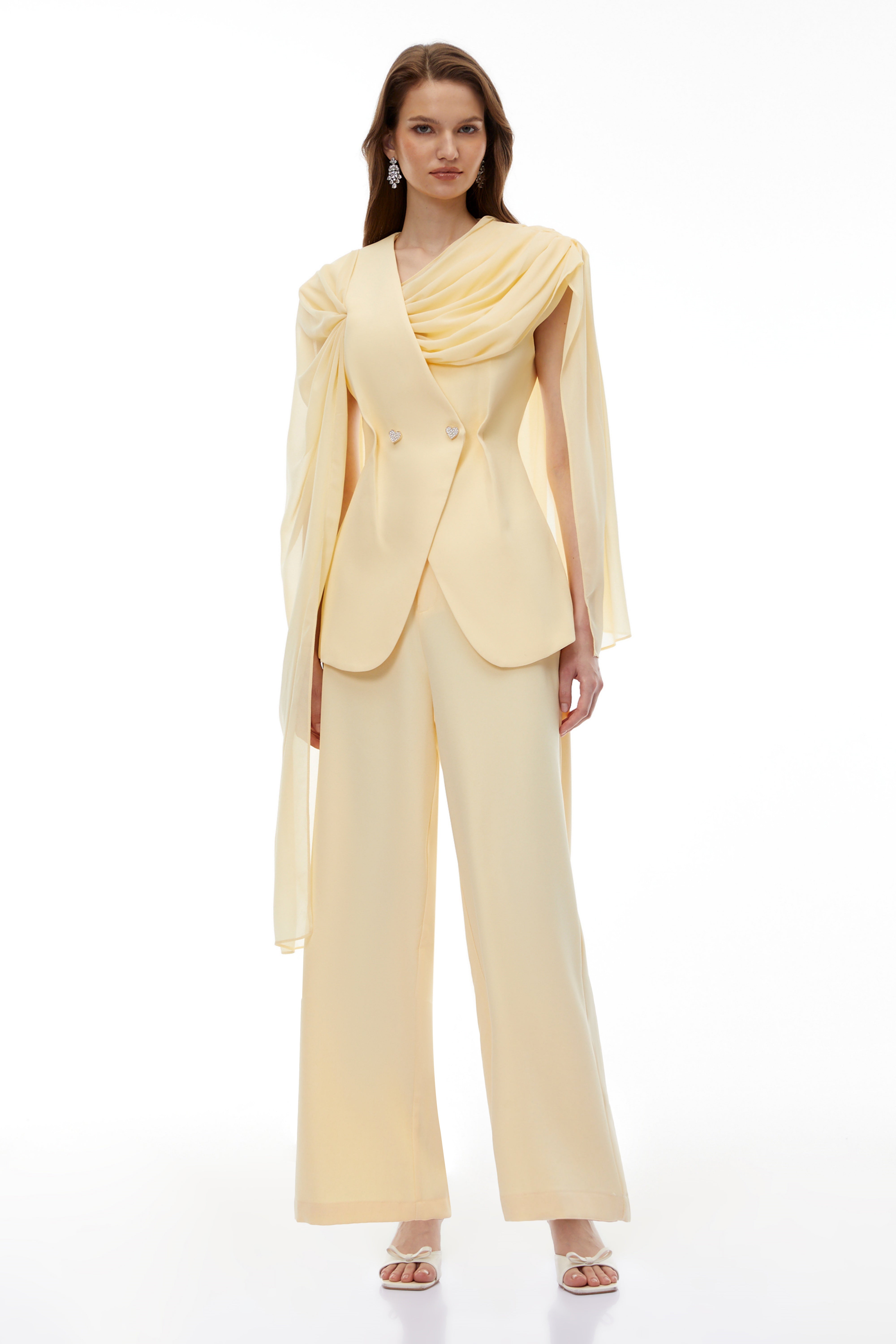 Pale yellow top and trousers set with an asymmetric blazer bodice, draped sheer neckline, and cape panels