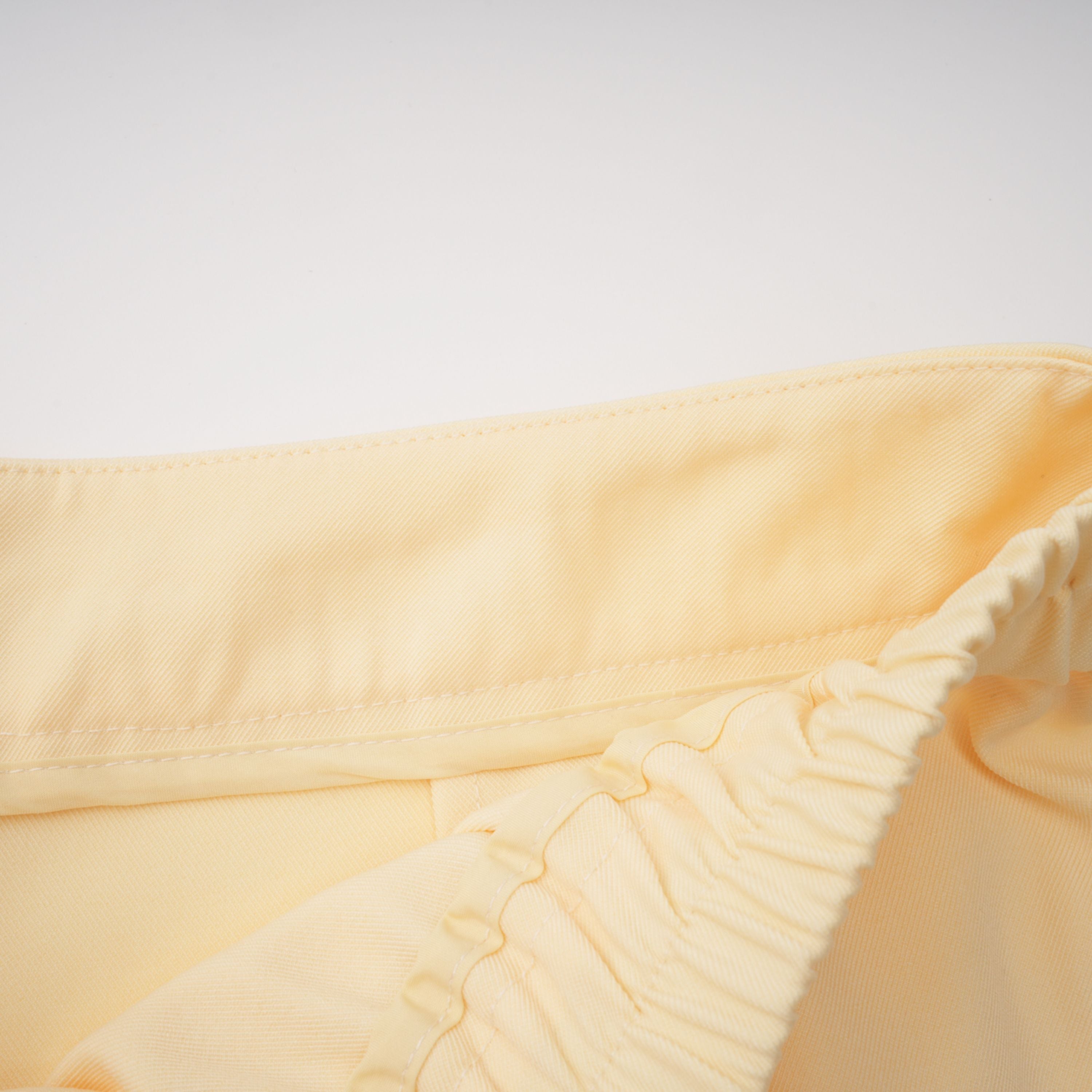 Pale yellow top and trousers set with an asymmetric blazer bodice, draped sheer neckline, and cape panels