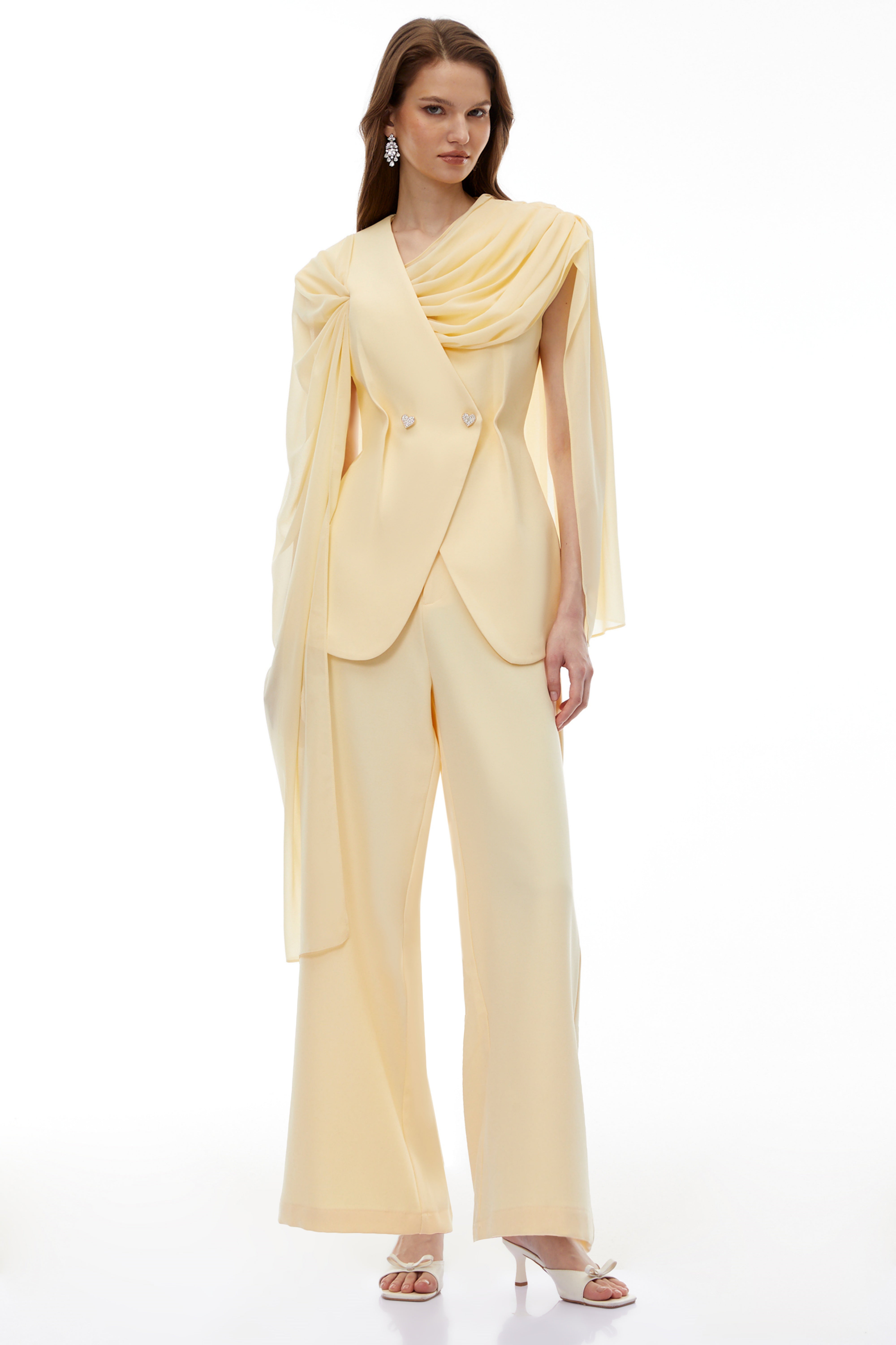 Pale yellow top and trousers set with an asymmetric blazer bodice, draped sheer neckline, and cape panels